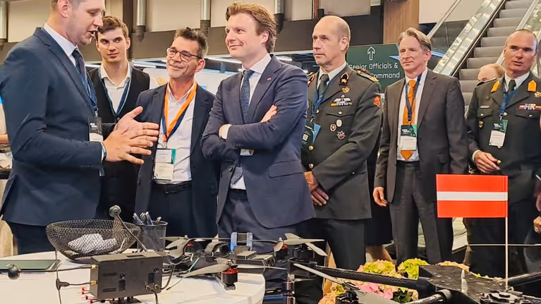 Brekelmans en anderen luisteren bij tafel met drone naar uitleg.